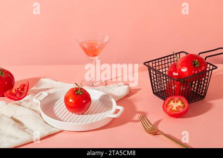 Auf rosafarbenem Hintergrund gibt es frische Tomaten, einen Korb aus Drahtgeflecht, ein Keramiktablett, ein Cocktailglas und ein Handtuch. Bereich für die Anzeige von Produkten mit mA Stockfoto