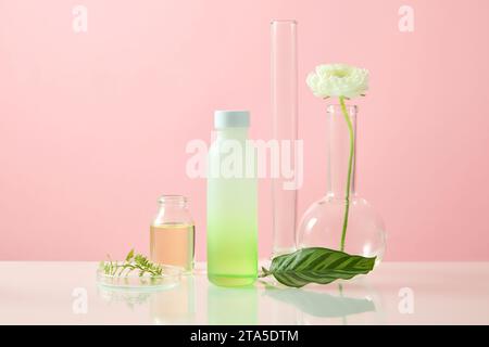 Laborkonzept mit einer leeren Etikettenflasche, die mit einer Petrischale und anderen Gläsern angeordnet ist. Forschungs- und Entwicklungskosmetikkonzept. Rosafarbenes Backgro Stockfoto