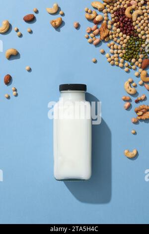 Verschiedene Arten von Nüssen und Bohnen sind auf blauer Oberfläche mit einer leeren Flasche Milch verziert. Draufsicht. Leeres Etikett für Produktmodell Stockfoto