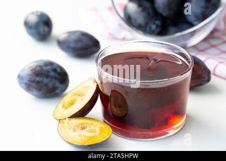 Hausgemachte Pflaumenmarmelade in blauer Keramikschale und Beeren auf weißem hölzernem Hintergrund. Stockfoto