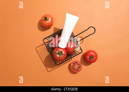 Ein Korb mit frischen Tomaten, auf dem ein unbeschrifteter Korb steht. Orangefarbener Hintergrund. Der Gehalt an Vitamin-B-Komplex in Tomaten hilft bei der Bekämpfung Stockfoto