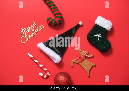 Einige niedliche dekorative Objekte mit vielen Bedeutungen für Weihnachten sind auf einem roten Hintergrund zu sehen. Hüte und Stock von Santa Claus, Rentier, Zuckerrohr A Stockfoto