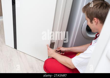 Bohren und Einbau von Innentüren, macht der Handwerker ein Loch in den Türrahmen mit einem Handbohrer, Türen und Montage. Stockfoto