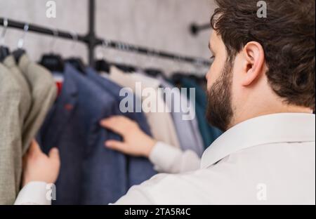 Mann, der eine Jacke aus einem Kleiderständer in einem Geschäft auswählt Stockfoto