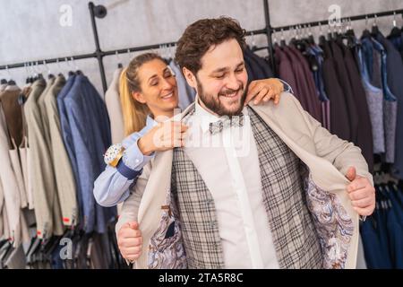 Ein Schneider hilft einem Mann, eine Jacke in einer Boutique anzuprobieren, beide lächeln Stockfoto