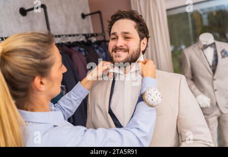 Schneiderei, die den Kragen eines Mannes in einem Anzug-Shop anpasst, beide lächeln Stockfoto