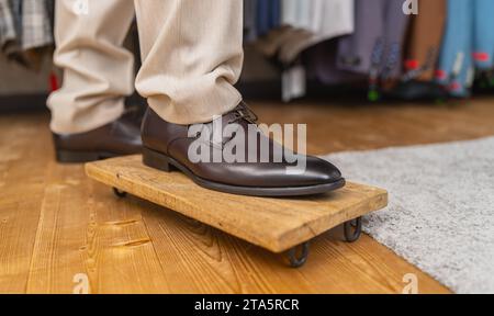 Mann, der braune Lederschuhe anprobiert, auf einem Fuß auf einem Holzbrett steht Stockfoto