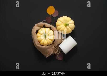 Festliches Herbstdekor aus Kürbissen in Sackleinen-Beutel, trockenen Blättern und weißer Kerze auf schwarzem Hintergrund. Konzept des Thanksgiving-Tages oder Halloween. Flache Lagen Stockfoto