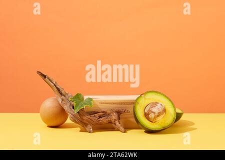 Szene für Werbung für Kosmetik mit Leerraum für Präsentationskosmetik. Frische Avocadohälften mit trockenem Zweig und Holzpodium o Stockfoto