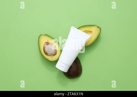 Beauty-Kräuter-Hautpflege und Haarpflegekonzept. Auf grünem Hintergrund, eine Plastikröhre mit frischen Avocadoscheiben verziert. Modell für Verpackung Stockfoto