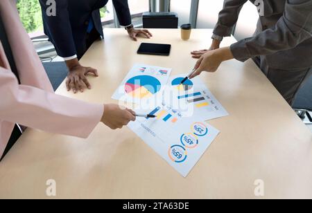 Eine Gruppe von Geschäftsleuten versammelt sich an einem Tisch und konzentriert sich auf verschiedene Diagramme und Datenvisualisierungen. Stockfoto