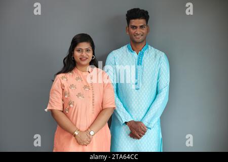 Fröhlicher indischer Mann und Frau in traditionellen Kleidern, die vor grauer Wand stehen Stockfoto