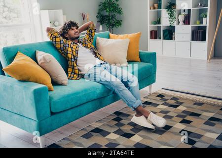 Ganzkörperfoto von gesinnter, fröhlicher Person sitzen Couch Hände hinter Kopf Tagträumend modernes Innenleben Wohnzimmer Haus drinnen Stockfoto