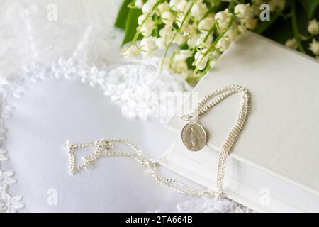 Erste Heilige Kommunion mit heiliger Medaille auf Kette und Blumen, Konzepthintergrund Stockfoto