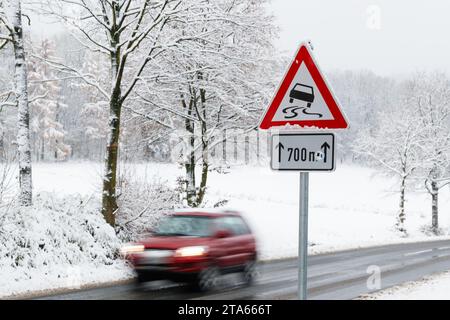 Bielefeld, Deutschland. November 2023. Ein Auto fährt auf einer Straße, auf der ein Verkehrsschild eine Rutsch- und Rutschgefahr anzeigt. Das Wetter in weiten Teilen Nordrhein-Westfalens ist winterlich mit Schneefall und Temperaturen rund um den Gefrierpunkt. Quelle: Friso Gentsch/dpa/Alamy Live News Stockfoto