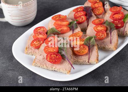 Hausgemachte Sandwiches mit putenpastete und Kirschtomaten sowie eine Tasse Kaffee auf grauem Hintergrund Stockfoto