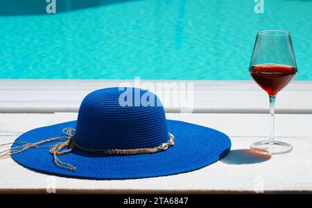 Sommerhut und ein Glas Wein vor dem Pool. Urlaubskonzept. Stockfoto