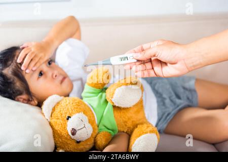 Mutter Eltern überprüfen die Temperatur ihrer kranken Tochter mit einem Digitalthermometer im Mund Stockfoto