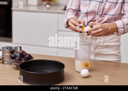 Weibliche Hände brechen Eier zum Backen in der modernen Küche Stockfoto