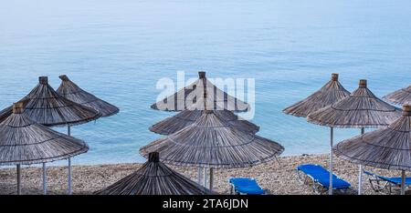 Strohschirme und Liegen am Strand. Leerer Strand mit Sonnenschirmen und Liegen. Strand ohne Leute. Konzeptidee für Urlaub, Urlaub Stockfoto