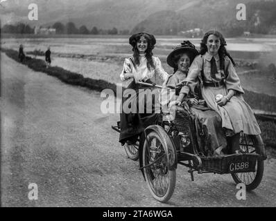 Drei viktorianische Mädchen aus der Oberschicht fahren in den 1890er Jahren mit ihrem Dreirad eine Landstraße hinunter Stockfoto