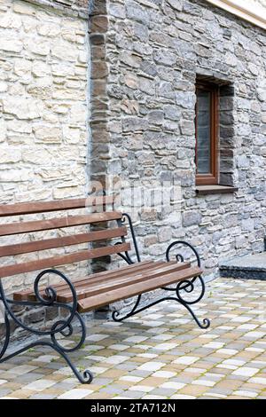 Eine Bank mit schmiedeeisernen Geländern vor dem Hintergrund einer strukturierten Steinmauer eines Hauses am Tag. Stockfoto