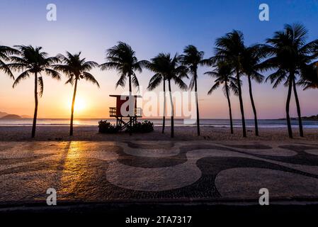 Palmen und Rettungsschwimmerposten am Copacabana Beach am Sonnenaufgang und berühmtem Bürgersteig Mosaic Stockfoto