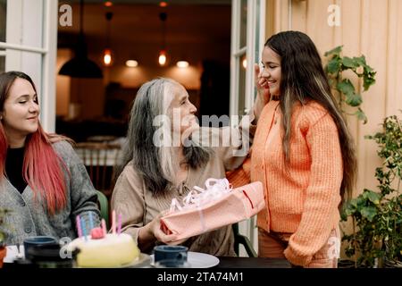 Seniorin hält Geburtstagsgeschenk von Enkelin auf der Terrasse Stockfoto