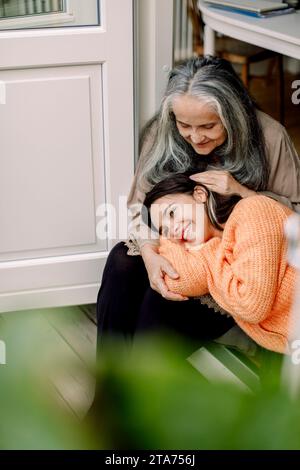 Glückliche Seniorin streichelt ihre Enkelin, während sie vor der Tür sitzt Stockfoto
