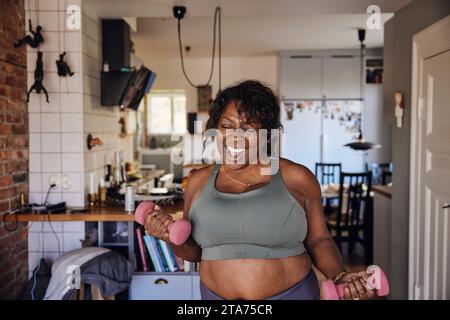 Fröhliche reife Frau, die zu Hause mit Kurzhanteln tanzt und trainiert Stockfoto