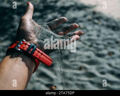 Schwarzer Sand als Hintergrund. Hände halten Sand in dunklem Hintergrund. Black Sand Beach, Langkawi, Malaysia. Hände einer Frau, die schwarzen Sand vom Strand aufnimmt Stockfoto