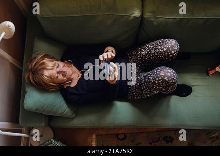 Direkt über dem Schuss einer älteren Frau, die ihr Mobiltelefon benutzt, während sie zu Hause auf dem Sofa liegt Stockfoto