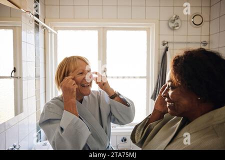 Glückliche multirassische Freundinnen, die Hautpflege zusammen im Badezimmer zu Hause machen Stockfoto
