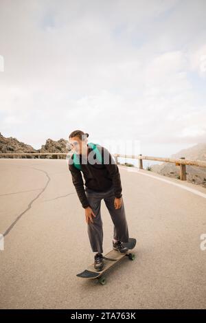 Junger Mann, der im Urlaub auf der Straße gegen den Himmel fährt Stockfoto