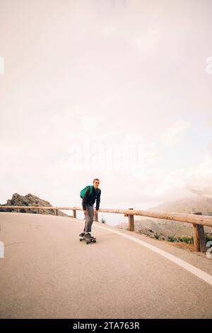 Junger Mann Skateboarding in der Nähe von hölzernen Leitplanken auf der Straße gegen den Himmel Stockfoto