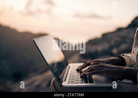 Hände einer Frau, die bei Sonnenuntergang im Urlaub auf einem Laptop tippt Stockfoto