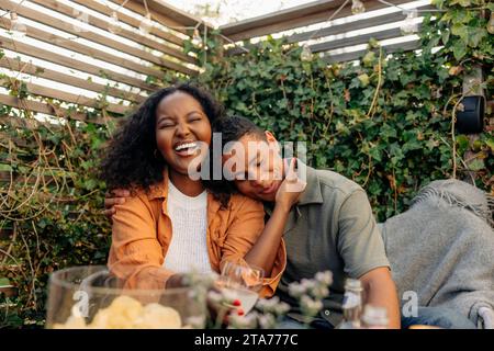 Glückliche junge Frau, die mit einem lächelnden männlichen Freund auf der Party sitzt Stockfoto