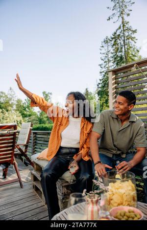 Junge Frau winkt, während sie mit einem männlichen Freund während der Party sitzt Stockfoto