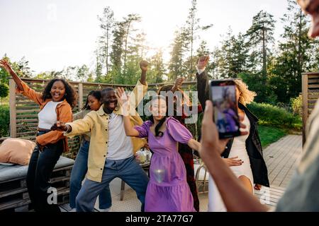 Mann fotografiert fröhliche männliche und weibliche Freunde, die während der Party im Hinterhof tanzen Stockfoto
