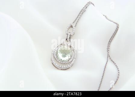 Ein luxuriöser Anhänger aus Weißgold mit einem zentralen grünen Amethyst-Edelstein, umgeben von einem funkelnden Diamanten, präsentiert an einer zarten Kette Stockfoto