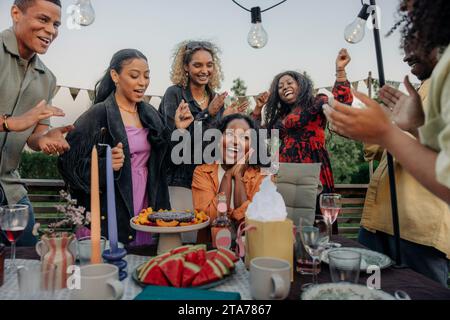 Fröhliche männliche und weibliche Freunde applaudieren der jungen Frau, während sie im Hinterhof Geburtstag feiern Stockfoto