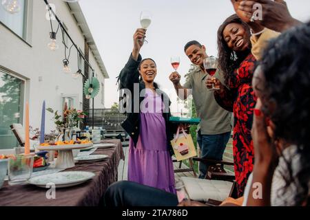 Glückliche männliche und weibliche Freunde, die im Hinterhof Drinks trinken Stockfoto