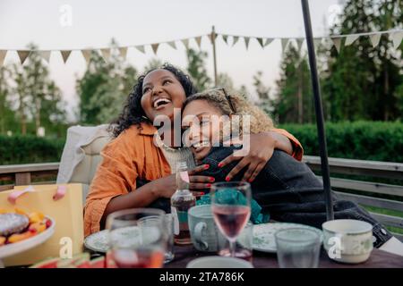 Lächelnde Frau, die eine Freundin bei der Geburtstagsfeier im Hinterhof umschließt Stockfoto