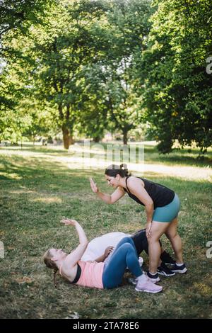 Seitenansicht einer Coach-Frau, die High-Five für eine Frau gibt, die auf Gras im Park liegt Stockfoto