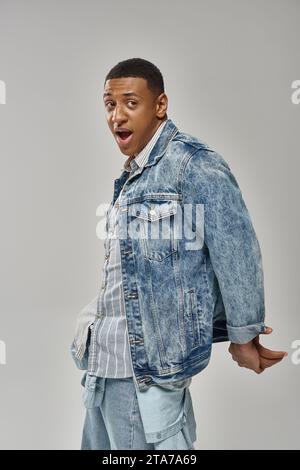 Schockierter emotionaler afroamerikanischer Mann in stilvollem Denim-Outfit mit lebendigem Modekonzept Stockfoto