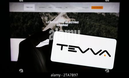 Person mit Smartphone und Logo des britischen Elektrolastwagenunternehmens Tevva Motors Limited vor der Website. Schwerpunkt auf dem Display des Telefons. Stockfoto