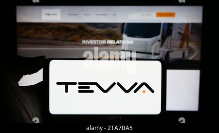Person, die ein Mobiltelefon mit dem Logo des britischen Elektrolastwagenunternehmens Tevva Motors Limited vor der Webseite hält. Schwerpunkt auf dem Display des Telefons. Stockfoto