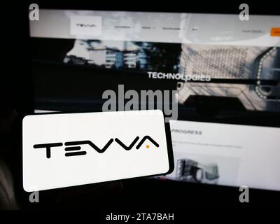Person, die ein Mobiltelefon mit dem Logo des britischen Elektrolastwagenunternehmens Tevva Motors Limited vor der Website des Unternehmens hält. Schwerpunkt auf dem Display des Telefons. Stockfoto