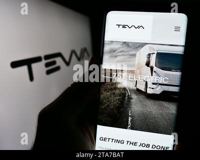 Person mit Mobiltelefon mit Website des britischen Elektrolastwagenunternehmens Tevva Motors Limited mit Logo. Konzentrieren Sie sich auf die Mitte des Telefondisplays. Stockfoto