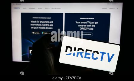 Person, die ein Mobiltelefon mit dem Logo des US-amerikanischen Fernsehverteilers DirecTV LLC vor der Website des Unternehmens hält. Schwerpunkt auf dem Display des Telefons. Stockfoto